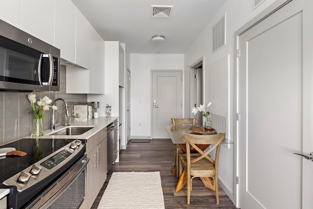 kitchen with dark wood-type flooring, white cabinets, sink, tasteful backsplash, and stainless steel appliances