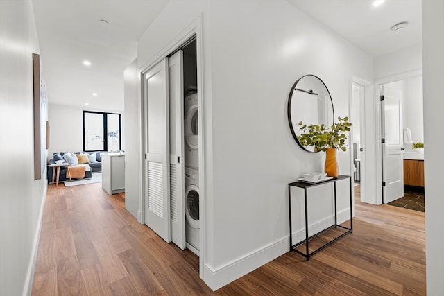 corridor with stacked washing maching and dryer and hardwood / wood-style flooring