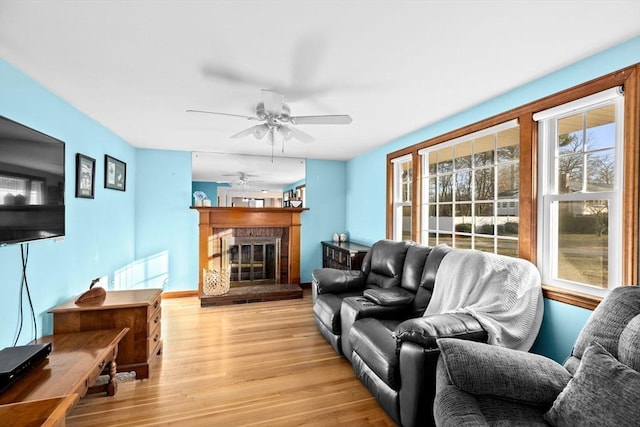 living room featuring a fireplace, light wood-type flooring, and ceiling fan