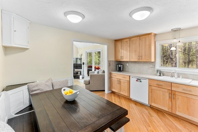 kitchen with light brown cabinetry, white dishwasher, a sink, and light countertops