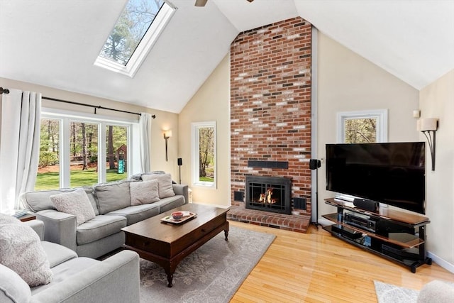 living area with a fireplace, wood finished floors, a skylight, and high vaulted ceiling