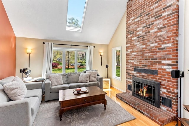 living area featuring visible vents, wood finished floors, a fireplace, high vaulted ceiling, and a skylight