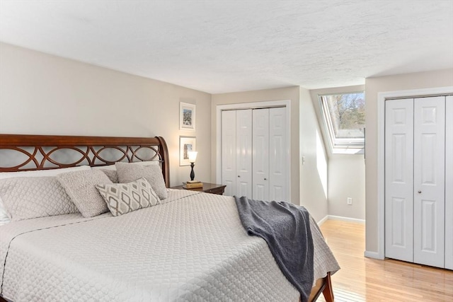bedroom featuring baseboards, multiple closets, and light wood-style flooring