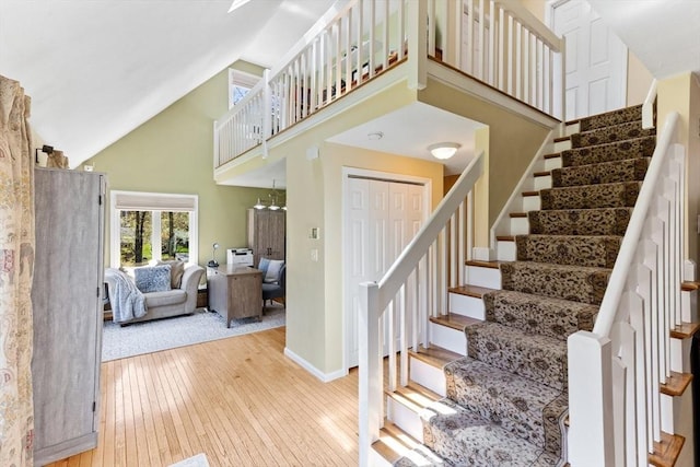 stairway with baseboards, hardwood / wood-style floors, and high vaulted ceiling