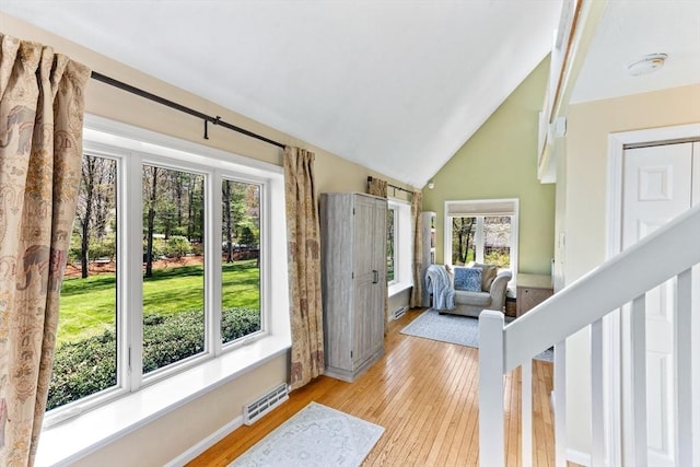 doorway with light wood-style floors, baseboards, vaulted ceiling, and visible vents