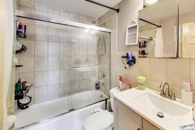 full bathroom featuring toilet, combined bath / shower with glass door, vanity, tile walls, and decorative backsplash