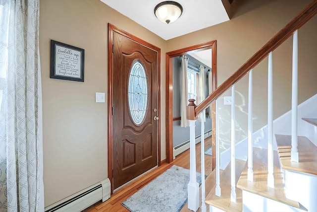 foyer entrance with a baseboard heating unit, stairway, and wood finished floors