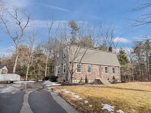 colonial inspired home featuring brick siding, a shingled roof, a front yard, a chimney, and driveway