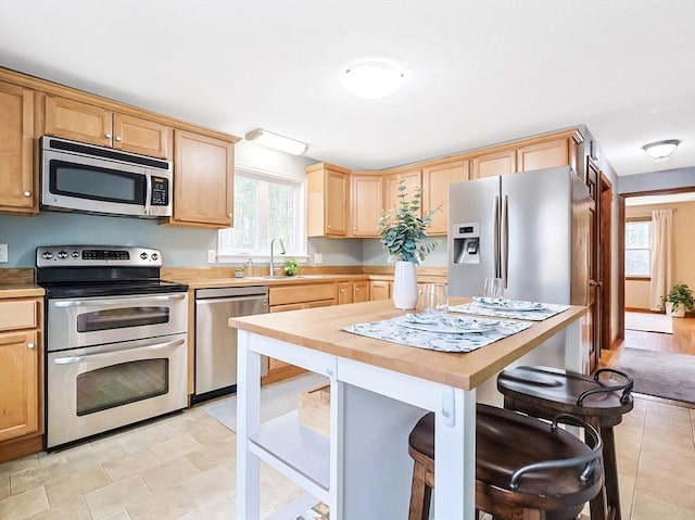 kitchen featuring light brown cabinets, butcher block counters, a breakfast bar area, appliances with stainless steel finishes, and a sink