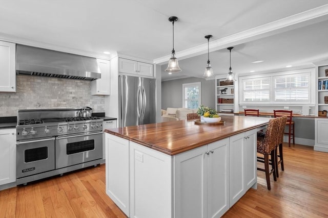 kitchen with white cabinetry, appliances with stainless steel finishes, a kitchen island, pendant lighting, and wall chimney range hood