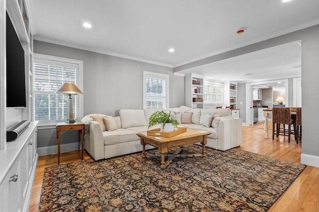 living room featuring built in features, light hardwood / wood-style flooring, and ornamental molding