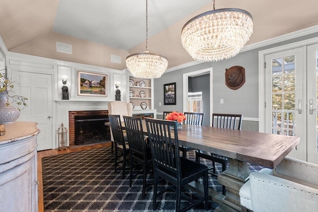 dining room with a notable chandelier, ornamental molding, a brick fireplace, vaulted ceiling, and french doors