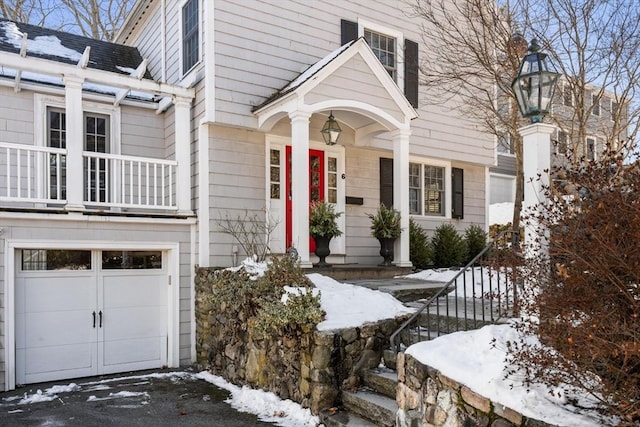 snow covered property entrance featuring a garage and a balcony