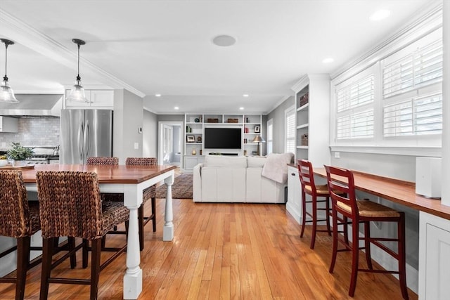 kitchen with hanging light fixtures, stainless steel refrigerator, ornamental molding, light hardwood / wood-style floors, and white cabinets