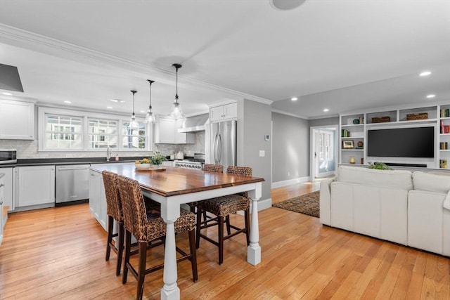 kitchen featuring sink, white cabinetry, pendant lighting, stainless steel appliances, and wall chimney range hood