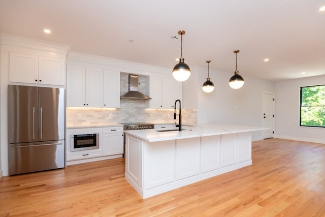 kitchen featuring sink, stainless steel appliances, a kitchen island with sink, and wall chimney range hood