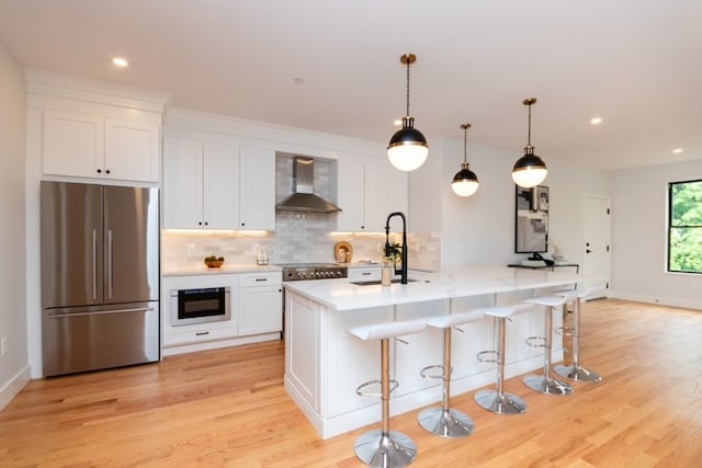 kitchen with a kitchen island with sink, white cabinetry, stainless steel appliances, and wall chimney range hood