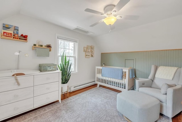 bedroom featuring a crib, ceiling fan, vaulted ceiling, wood finished floors, and a baseboard radiator