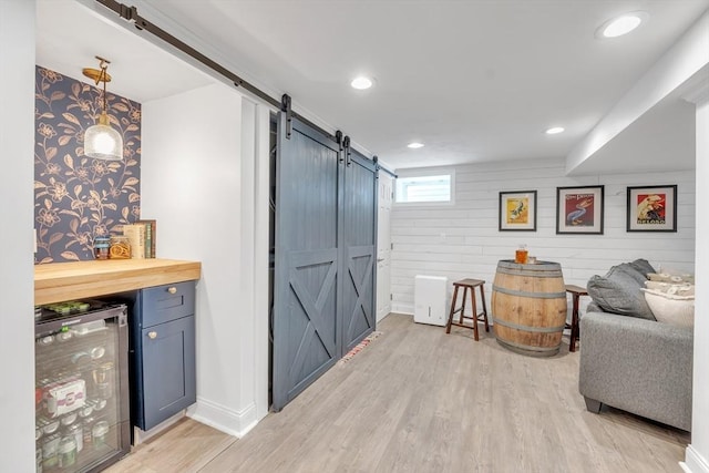 bar with beverage cooler, recessed lighting, a barn door, light wood finished floors, and baseboards