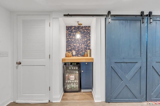 bar featuring light wood-type flooring, a barn door, baseboards, and a dry bar