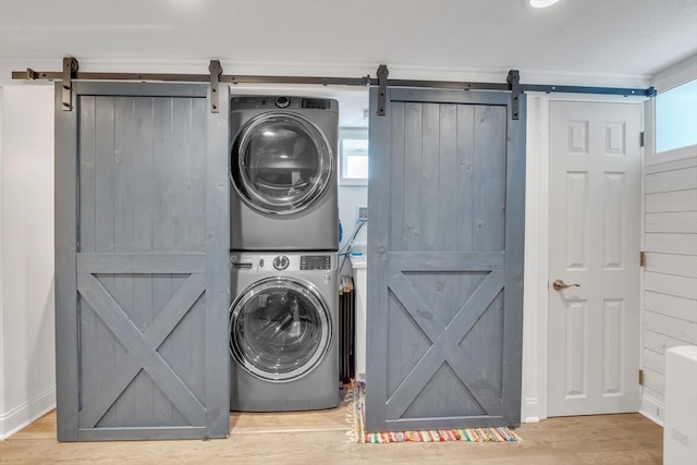 washroom with stacked washer / dryer, laundry area, a barn door, and wood finished floors