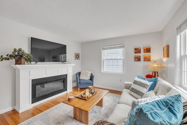 living area with baseboards, a glass covered fireplace, and light wood finished floors