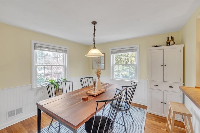 dining space featuring light wood-type flooring, visible vents, and wainscoting