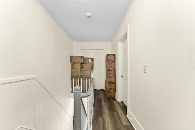 hallway with a textured ceiling, a decorative wall, dark wood-style floors, and an upstairs landing