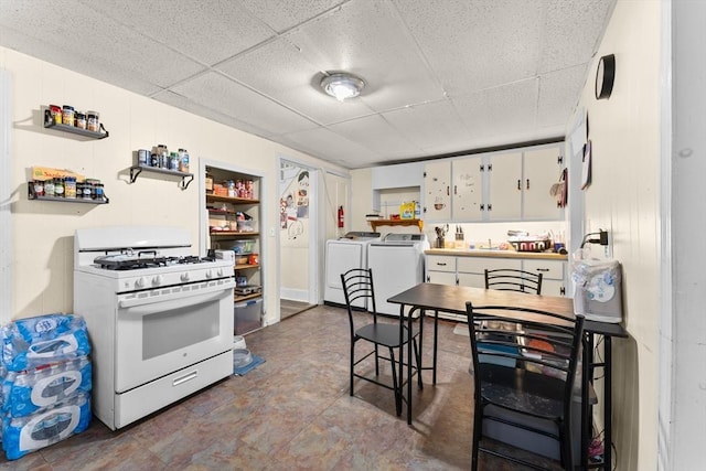 kitchen with open shelves, a drop ceiling, white gas stove, washing machine and clothes dryer, and a sink
