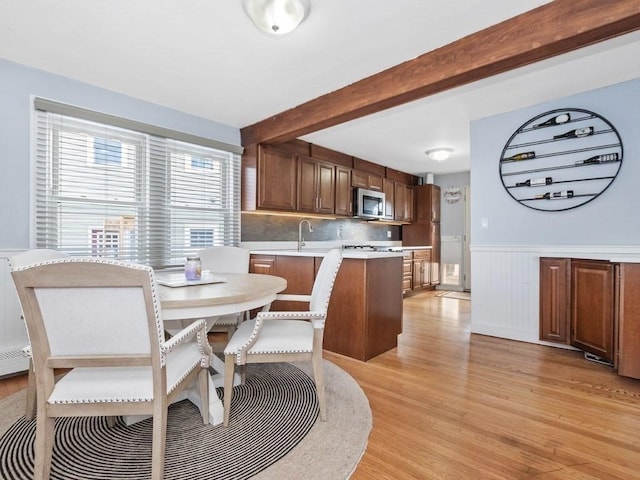 dining room with light wood-type flooring, a wainscoted wall, and beamed ceiling