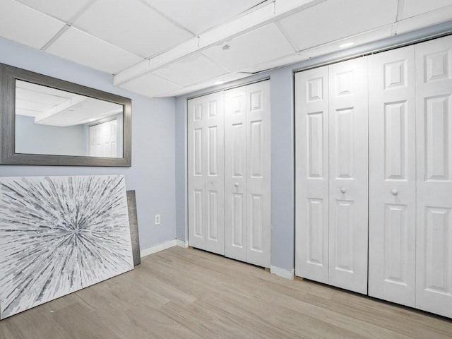 unfurnished bedroom featuring a paneled ceiling, baseboards, multiple closets, and wood finished floors