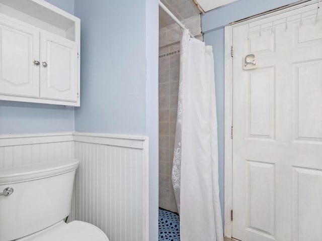 bathroom with a wainscoted wall, a stall shower, and toilet