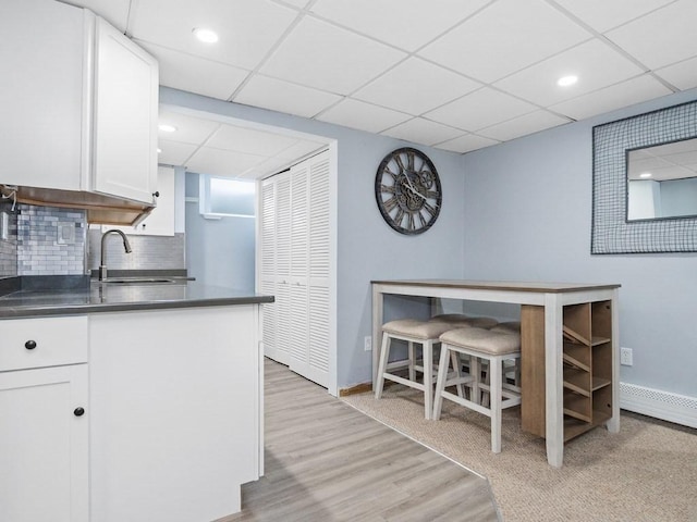 kitchen with dark countertops, decorative backsplash, white cabinets, a sink, and light wood-type flooring