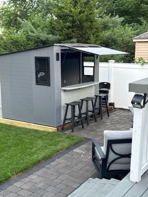 view of outdoor structure with fence, outdoor dry bar, and an outbuilding