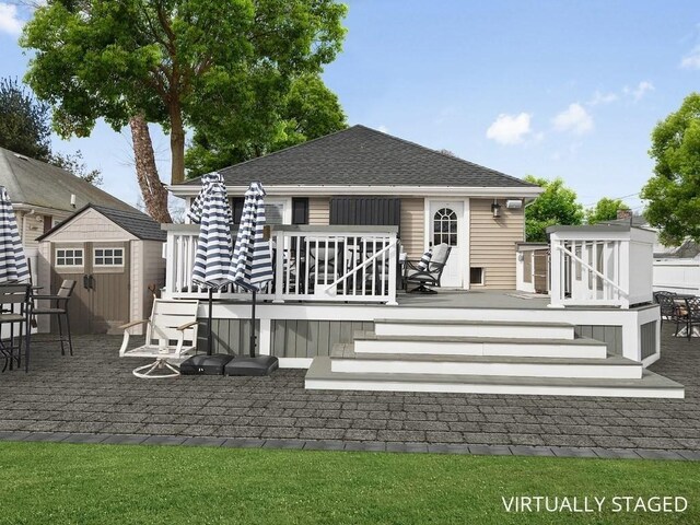 back of house with a storage shed, a wooden deck, roof with shingles, and an outdoor structure