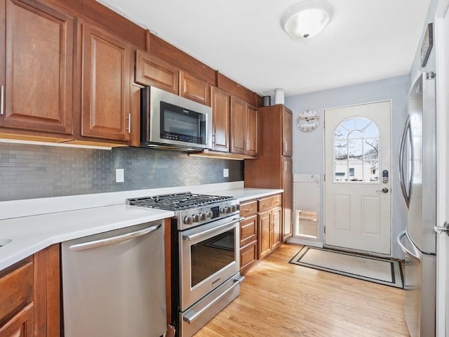 kitchen featuring brown cabinets, light wood finished floors, stainless steel appliances, light countertops, and decorative backsplash