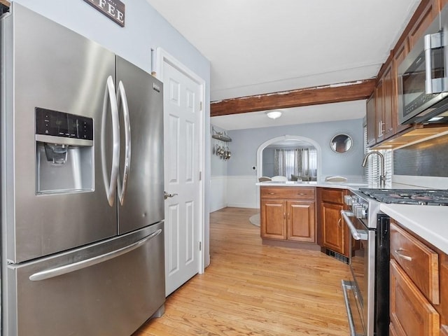 kitchen featuring arched walkways, light wood-style flooring, a peninsula, stainless steel appliances, and light countertops