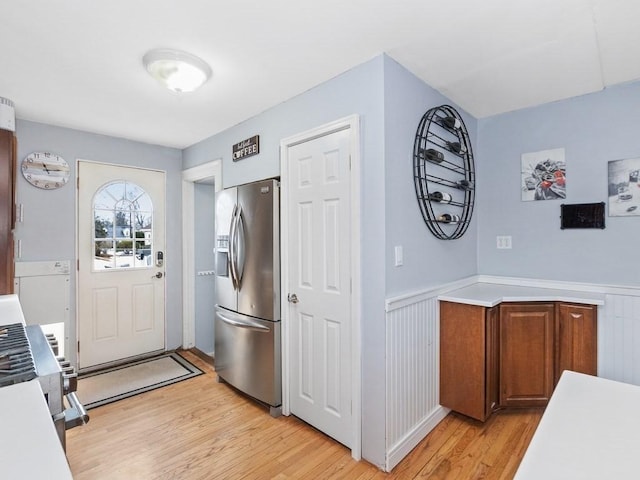 kitchen featuring a wainscoted wall, appliances with stainless steel finishes, light wood-type flooring, and brown cabinets