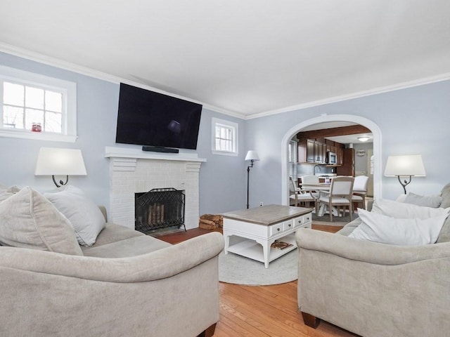 living area with light wood-type flooring, arched walkways, a fireplace, and crown molding