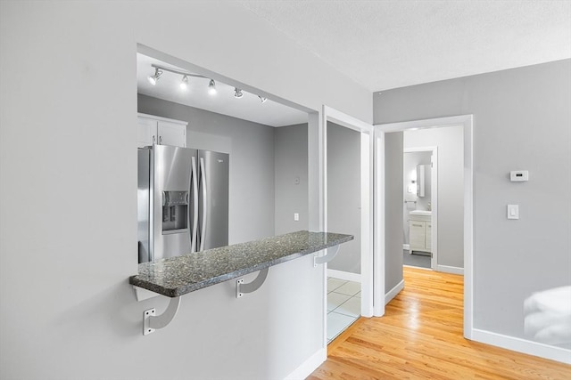 11 Cogswell Ave Unit 16, Cambridge, MA 02140 - kitchen with stainless steel fridge with ice dispenser, white cabinetry, a breakfast bar, light wood finished floors, and baseboards