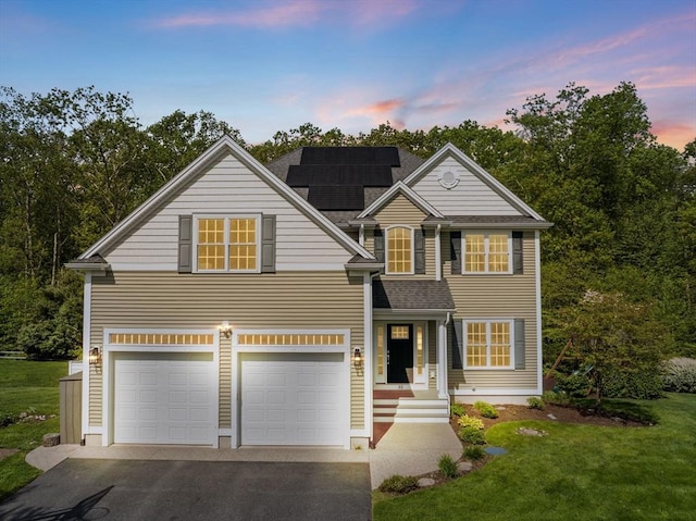 traditional-style home featuring a garage, asphalt driveway, solar panels, a lawn, and a shingled roof