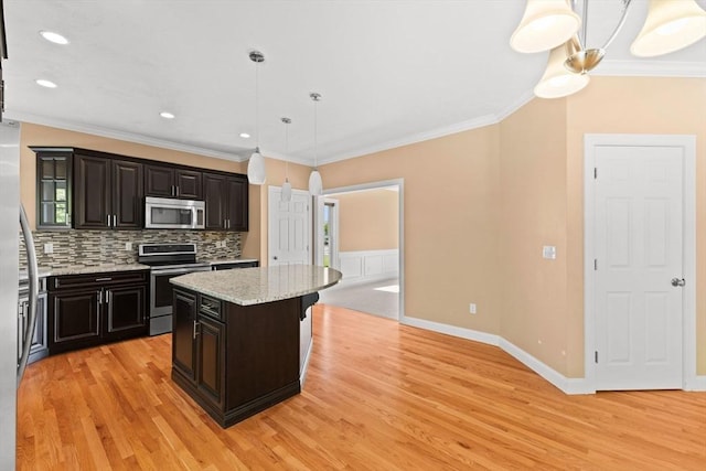 kitchen with appliances with stainless steel finishes, light wood-style flooring, crown molding, decorative backsplash, and a kitchen island