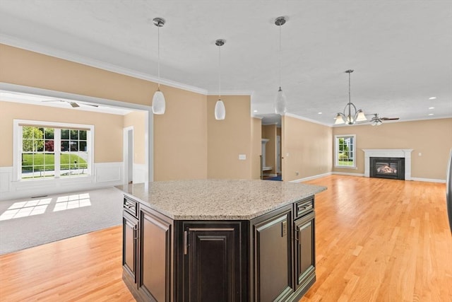 kitchen featuring open floor plan, light wood-style floors, hanging light fixtures, healthy amount of natural light, and a wainscoted wall