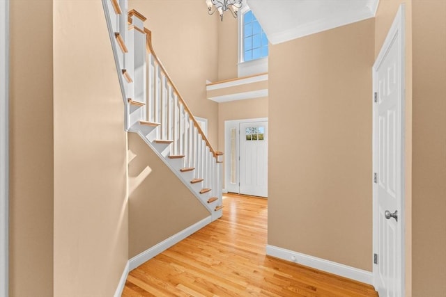 foyer entrance featuring baseboards, stairway, wood finished floors, a towering ceiling, and a chandelier