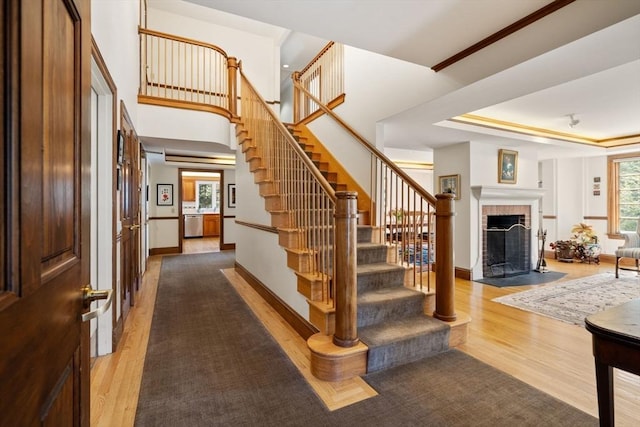 stairs with baseboards, a tray ceiling, a fireplace, a towering ceiling, and wood finished floors