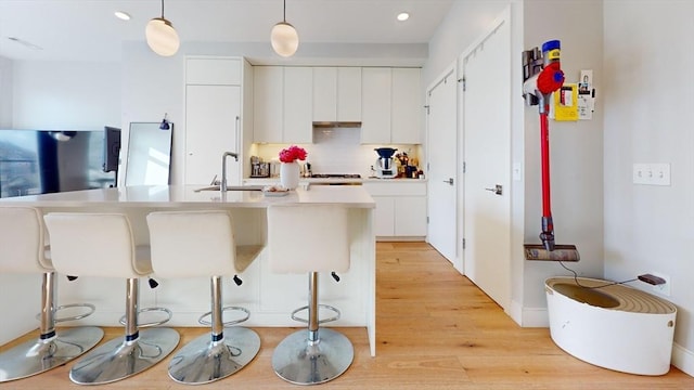 kitchen featuring a breakfast bar area, sink, white cabinets, and decorative light fixtures