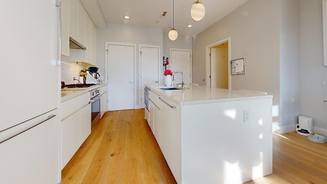 kitchen featuring sink, pendant lighting, white cabinets, and an island with sink