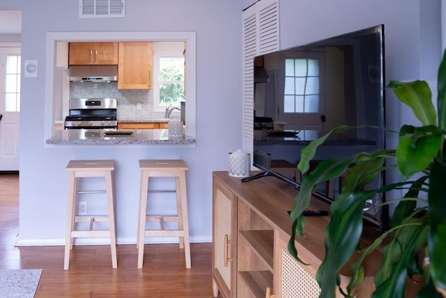 62 Roberts Dr Unit 62, Bedford, MA 01730 - kitchen featuring stainless steel stove, wood finished floors, backsplash, and exhaust hood