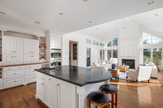 kitchen with vaulted ceiling, a center island with sink, white cabinetry, and dark wood-type flooring