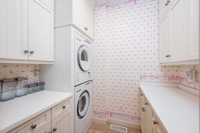 laundry area with cabinets, light tile patterned floors, and stacked washer and clothes dryer